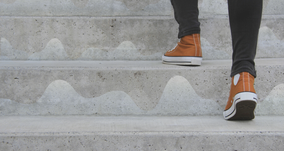 A person in orange high top sneakers is walking up concrete steps with line graphs representing data.